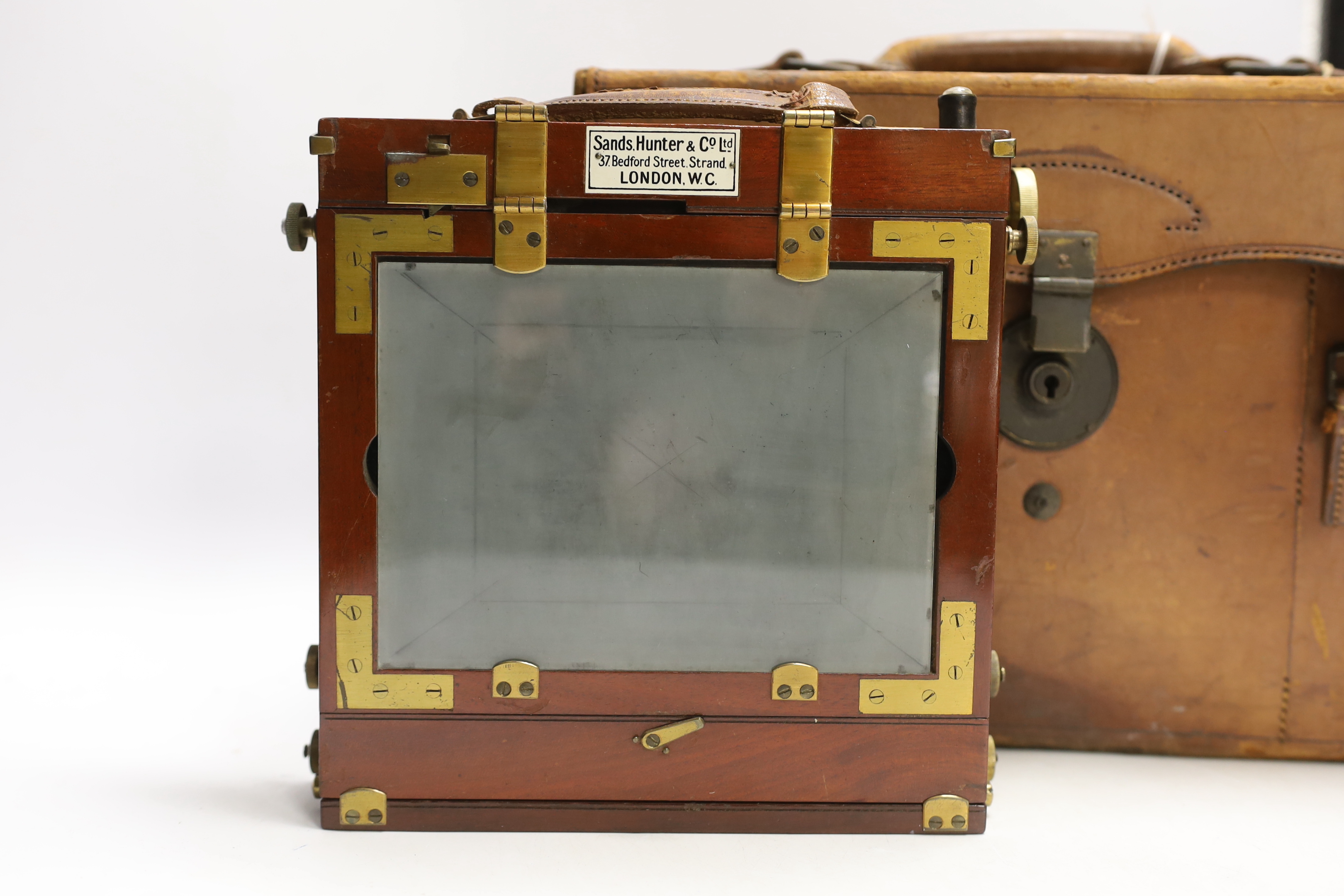 An early 20th century half plate camera by Sands, Hunter & Co. 37 Bedford Street, Strand, London WC, mahogany and brass frame, body 21 x 20cm, in the original leather case, also containing a Taylor, Taylor & Hobson Ltd.